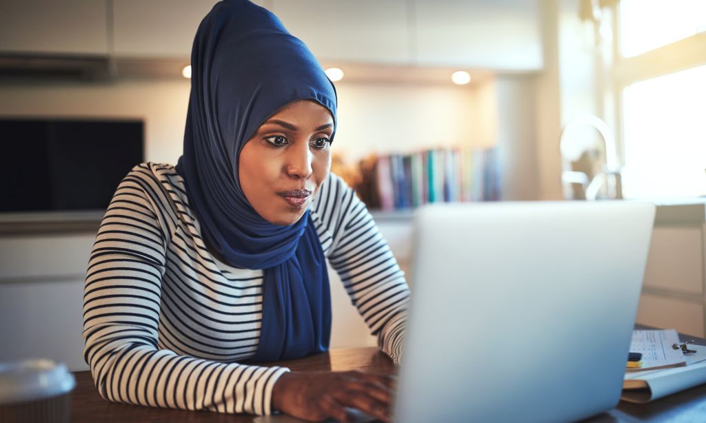 Eine Frau mit Hijab sitzt hinter ihrem aufgeklappten Laptop an einem Tisch