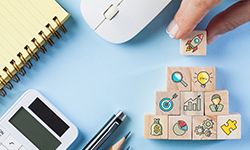 Holzwürfel mit bunten Icons zum Thema Startup liegen auf einem Untergrund mit verschiedenen Büroutensilien.